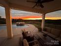 Cozy covered patio with comfortable seating, overlooking a beautiful pool and scenic landscape at sunset at 7248 Waterwheel Sw St, Concord, NC 28025