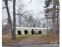 A single-level home featuring a gravel driveway lined with bushes and surrounded by leafless trees at 1926 Scenic Dr, Iron Station, NC 28080