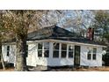 Quaint cottage-style home with black roof and white siding, nestled among mature trees in a quiet neighborhood at 7608 Kershaw Camden Hwy, Kershaw, SC 29067
