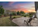 Beautiful backyard with a large patio, mature trees, and lush landscaping under a vibrant sunset sky at 7095 Sunset Crater Pl, Lancaster, SC 29720