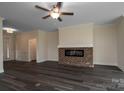 Open living room with a ceiling fan, fireplace with a brick hearth, and dark wood flooring, creating a warm ambiance at 3034 Buffet Ln, Monroe, NC 28110