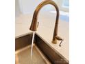 Close-up of a modern kitchen sink with a sleek bronze faucet and water running, paired with white countertop at 3111 Vermillion Dr, Harrisburg, NC 28075