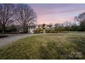 A stone and brick home has a manicured lawn and mature trees at dusk at 13031 Westmoreland Farm Rd, Davidson, NC 28036