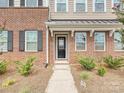 Charming townhome entrance featuring a brick facade, black door with sidelights, and mature landscaping at 114 Marron Dr, Indian Trail, NC 28079