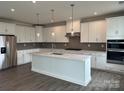 Modern white kitchen with stainless steel appliances, island, and gray backsplash at 7120 Wayfarer Dr # 0079, Charlotte, NC 28269
