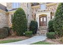 Stone and brick home featuring a beautiful arched wooden front door, stone steps, and manicured landscaping at 4008 Quintessa Dr, Matthews, NC 28104