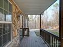 The covered porch features stone accents, wooden railing, and a view of the surrounding wooded landscape at 4775 Lands End Trl, Alexis, NC 28006