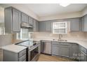 Well-lit kitchen featuring gray cabinets, stainless steel appliances, and a dual basin sink below a window at 8137 Sheringham Way, Charlotte, NC 28227