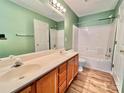 Bathroom featuring dual sinks, wood cabinets, and a shower-tub combo with green accent walls at 12906 Sickles Dr, Charlotte, NC 28273