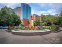 A circular brick fountain with cascading water surrounded by flowers and greenery in an urban setting at 210 N Church St # 3606, Charlotte, NC 28202