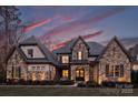 Stunning stone home with a dramatic roofline, highlighted by professional lighting and a colorful sunset at 17639 Stuttgart Rd, Davidson, NC 28036