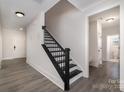 Bright hallway featuring a staircase with dark wood banister and gray wood flooring at 1308 Stone Marker Dr, Monroe, NC 28112