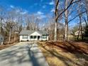 View of charming single-story home with a gray roof, white siding, and a spacious driveway surrounded by bare trees at 514 Meadowrock Dr, Albemarle, NC 28001