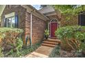 Close-up of a brick home featuring a red front door with detailed trim, complemented by lush landscaping at 12606 Bradford Hill Ln, Huntersville, NC 28078