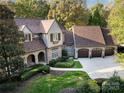 Aerial view of a two-story home with a three-car garage, manicured lawn, stone and siding, and mature trees at 1307 Wyndmere Hills Ln, Matthews, NC 28105