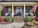 Inviting front porch with stone steps, elegant columns, seating area, and beautifully decorated double door entrance at 13114 Long Common Pkwy, Huntersville, NC 28078
