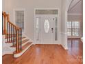 Elegant home foyer featuring a decorative front door, wooden staircase, and gleaming hardwood floors at 2100 Winding Oaks Trl, Waxhaw, NC 28173