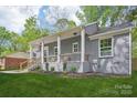 Charming gray brick home featuring a welcoming front porch with wooden railings, lush green lawn and manicured landscaping at 6813 Elm Forest Dr, Charlotte, NC 28212