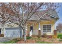 Inviting yellow house boasts a two-car garage, covered front porch, and a mature tree shading the landscaped yard at 1131 Curry Way # 69, Matthews, NC 28104