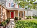 Inviting front porch with red front door, brick facade, and well-maintained landscaping at 10032 Montrose Nw Dr, Charlotte, NC 28269