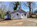 A grey house with a white front door and a detached outbuilding is surrounded by trees on a sunny day at 4924 Jane Ave, Charlotte, NC 28269