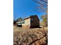 Side and back of beige home with green shutters and metal roof on a leaf covered lot at 191 Ashford Dr, Olin, NC 28660