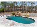 Backyard pool area with a rock waterfall feature and surrounding forest at 204 Silvercliff Dr, Mount Holly, NC 28120