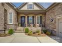 Covered front porch featuring stone pillars, two chairs, and lush landscaping at 14830 Creeks Edge Dr, Charlotte, NC 28278