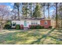 Charming single-story home with a brick and white facade, surrounded by lush greenery and mature trees at 1001 E 8Th Ave, Gastonia, NC 28054