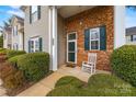 Cozy front porch with brick accent, a white rocking chair, and lush green bushes surrounding the entrance at 8830 Cinnabay Dr, Charlotte, NC 28216