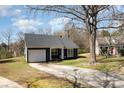 Quaint one-story home features a single-car garage, dark gray siding, and an expansive driveway at 12319 Delcorte Ln, Pineville, NC 28134