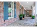Welcoming front porch with brick facade, stone flooring, shuttered windows, and potted ferns for added charm at 13822 Tributary Ct, Davidson, NC 28036