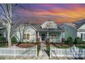 Inviting one-story home boasts a covered front porch, a classic white picket fence, and manicured landscaping at sunset at 7037 Ladys Secret Dr, Indian Trail, NC 28079