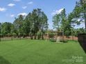 Large backyard with lush green grass, bordered by a black metal fence and a wooden playset at 518 Palmarosa St, Fort Mill, SC 29715