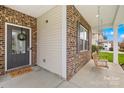 Covered front porch with brick accents, a small bench swing, and a welcoming entrance door with sidelights at 6126 Castlecove Rd, Charlotte, NC 28278