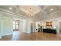 Bright open-plan living and kitchen space with coffered ceiling, hardwood floors, and modern chandelier at 102 Pecan Cove Ln, Weddington, NC 28104