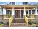 Inviting front porch with brick stairs, wood railings, and a stylish dark wood front door with glass panels at 116 S Broad St, Waxhaw, NC 28173