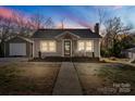 Charming single-story home at twilight featuring a welcoming front porch, well-maintained lawn, and separate single car garage at 108 S Buckoak St, Stanley, NC 28164