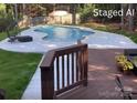 Backyard pool with deck and lounge seating surrounded by green grass and mature trees at 5672 Wrenfield Ct, Charlotte, NC 28277