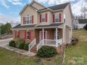 Inviting front of a two-story house with a mix of brick and siding, accentuated by red shutters and a cozy front porch at 5032 Meadow Woods Dr, Lowell, NC 28098