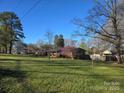 Expansive front yard view of a brick ranch-style home, featuring mature trees and lush green grass, inviting relaxation at 624 Patricia Ave, Harrisburg, NC 28075