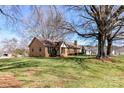 Spacious lawn surrounds this brick single-story home shaded by beautiful mature trees on a sunny day at 7770 Sherrills Ford Rd, Sherrills Ford, NC 28673