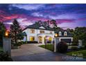 Elegant white brick home with a gated entrance, manicured landscaping, and warm exterior lighting at 16439 Jetton Rd, Cornelius, NC 28031