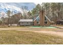 Charming two-story home with a brick chimney, metal roof, and gray siding, surrounded by lush greenery and mature trees at 360 Patience Dr, Concord, NC 28025