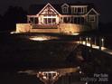 Exterior nighttime view of a large waterfront home with stone accents and a private dock at 5086 Windward Point Ln, Denver, NC 28037