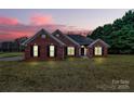 Charming single-story brick home featuring classic shutters and a well-manicured front lawn at dusk at 13930 Thompson Rd, Mint Hill, NC 28227