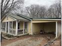 The home's exterior shows yellow siding, a metal roof, and a covered parking area next to a bare tree at 1140 Mt Vernon Rd, Woodleaf, NC 27054