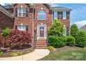 Striking brick home featuring a prominent entryway with a red door and manicured landscaping at 6141 Abergele Ln, Matthews, NC 28104