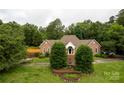 Inviting brick home features a lush front lawn with mature trees and a stone fountain at the base of the front steps at 105 Partridge Bluff Ne Dr, Concord, NC 28025