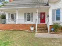 Inviting front porch with a brick base, red front door, and white swing for relaxing and enjoying the outdoors at 2602 Cherokee Ct, Gastonia, NC 28056